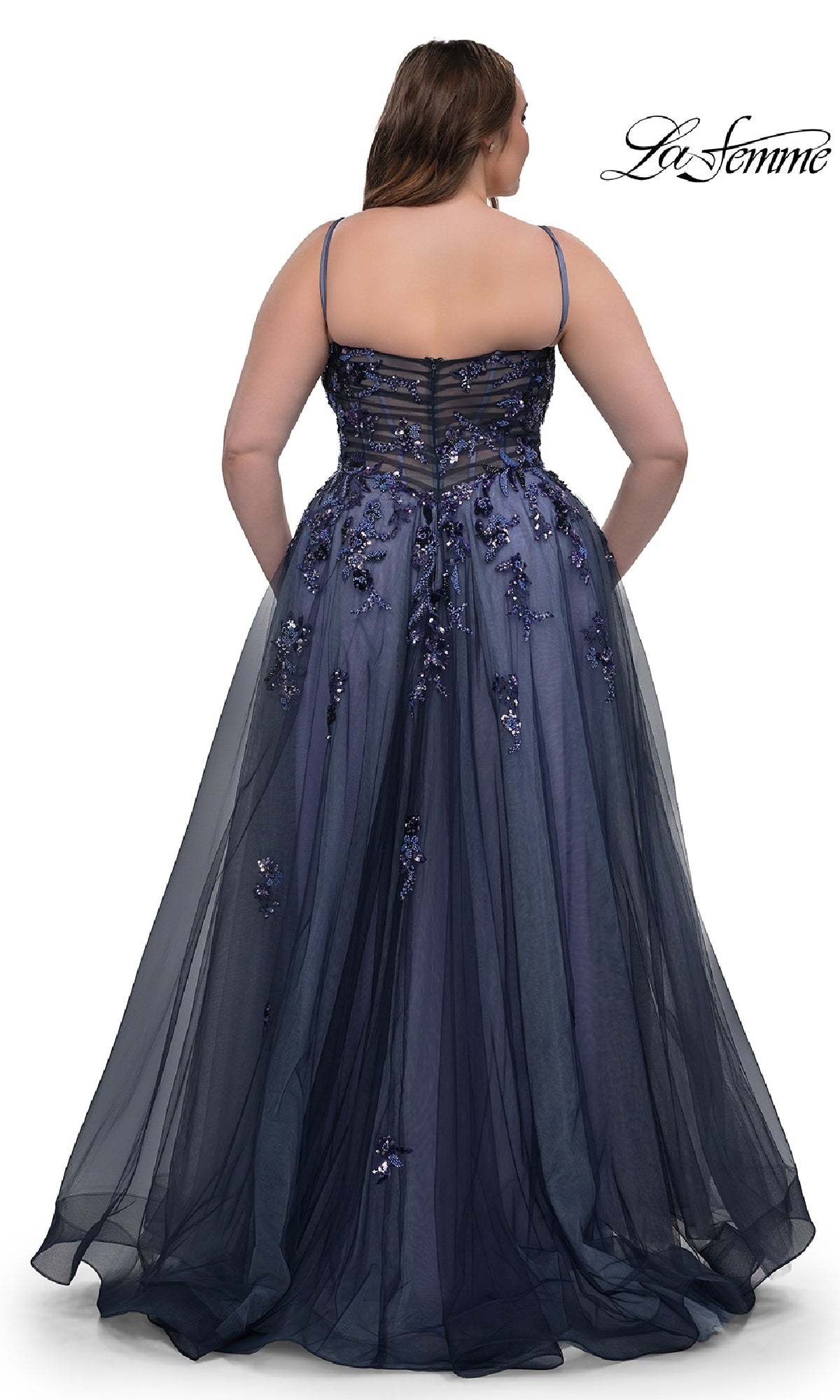 A woman showcases the La Femme 33061 navy plus-size prom dress from the back, featuring thin straps, sequin beaded floral appliqué, and a sheer overlay.